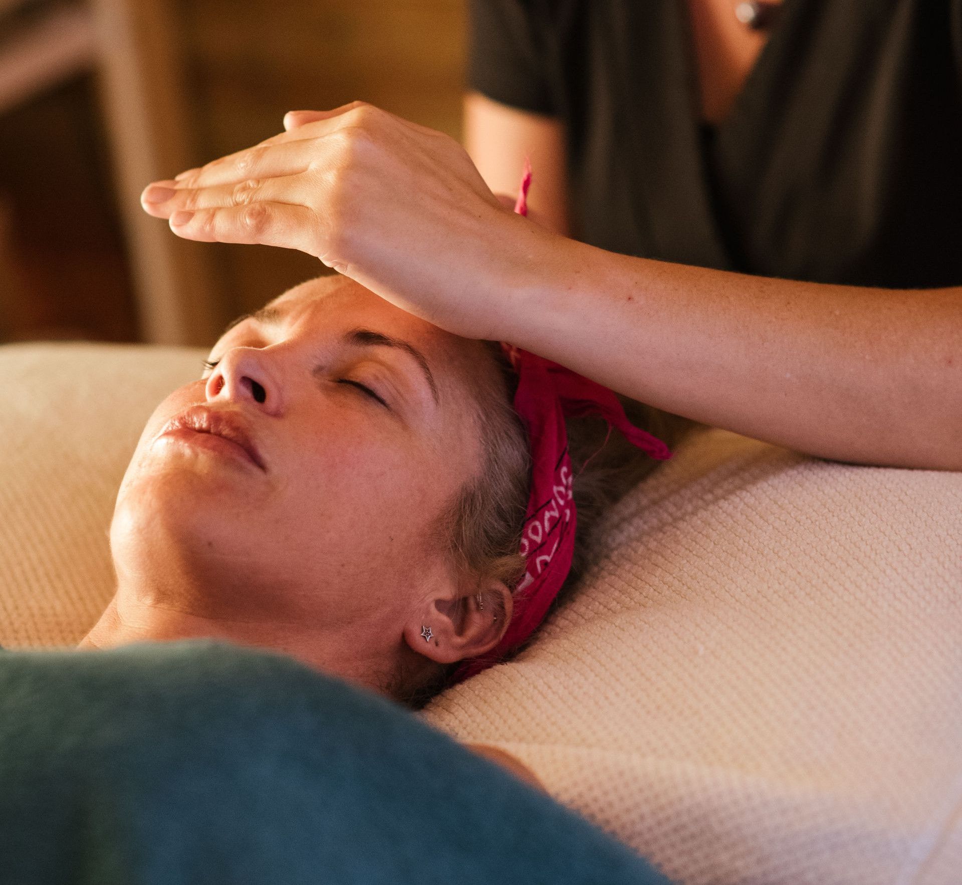 Relaxed woman with closed eyes lying under blanket while getting reiki therapy treatment from unrecognizable therapist in cozy salon with blurred background